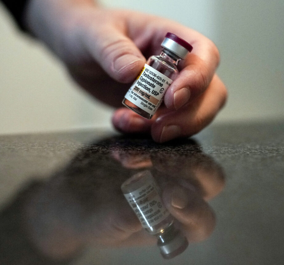 Ashton Colby holds a vial of Testosterone Cypionate Injection in his apartment bathroom in Columbus, Ohio, on Thursday, Jan. 18, 2024. Ohio Gov. Mike DeWine announced proposals this month that transgender advocates say could block access to gender-affirming care provided by independent clinics and general practitioners, leaving thousands of adults scrambling for treatment and facing health risks. Colby, 31, fears the clinic where he gets the testosterone he has taken since age 19 would no longer offer it. (AP Photo/Carolyn Kaster)